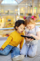 Obraz premium Little pretty girl and boy play with tablet pc on floor in mall.