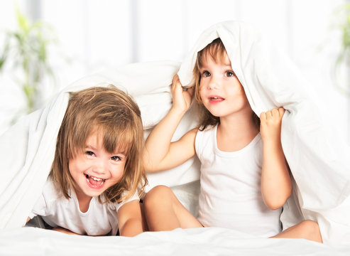 happy little girls twins sister in bed under the blanket having