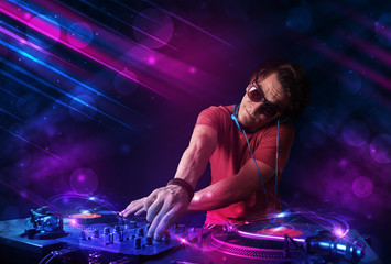 Young DJ playing on turntables with color light effects