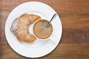 fresh croissant and cup of coffee on a plate on wooden table