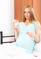 Pregnant woman holding thermometer and glass of water