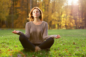 Beautiful young girl meditating in autumn park