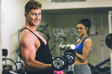 Fototapeta na wymiar Young man and woman using dumbbells in gym