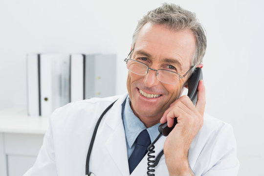 Smiling male doctor using telephone at office