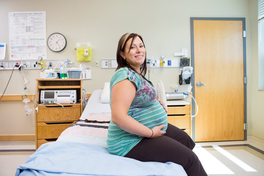 Happy Pregnant Woman With Hands On Stomach On Hospital Bed