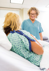 Happy Nurse Looking At Newborn Babygirl With Mother In Hospital