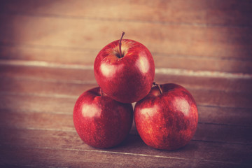 Three red apples on wooden table. Photo in retro color style.