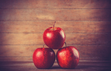 Three red apples on wooden table. Photo in retro color style.