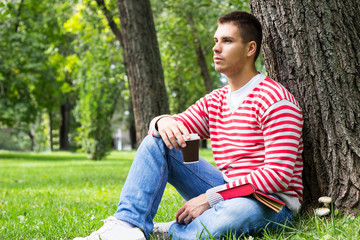Naklejka na ściany i meble Young man resting with a book and coffee to go