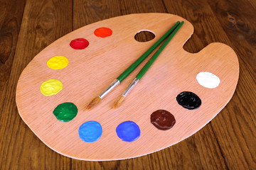Wooden art palette with paint and brushes on table close-up