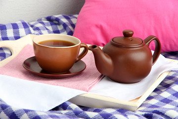 Cup and teapot on wooden tray on fabric background
