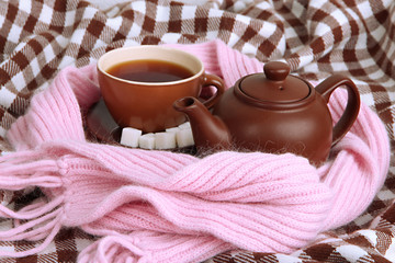 Cup and teapot with scarf on fabric background