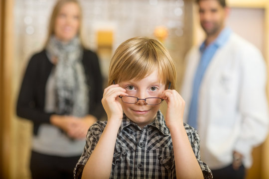 Boy Trying Eyeglasses With Optometrist And Mother At Store