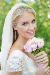 Obraz na płótnie Canvas Happy bride holding her bouquet smiling at camera