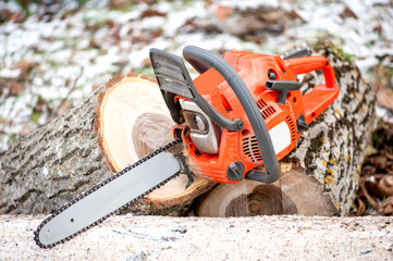 gasoline powered professional chainsaw on pile of cut wood