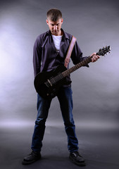 Fototapeta premium Young musician playing guitar on gray background
