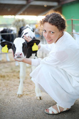 Woman in white robe caresses small calf and looks at camera