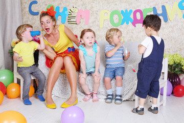 Four little kids with juice and entertainer sit on sofa - obrazy, fototapety, plakaty