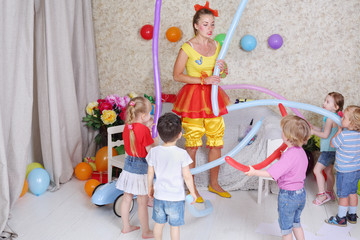 Five happy kids and facilitator play with long balloons