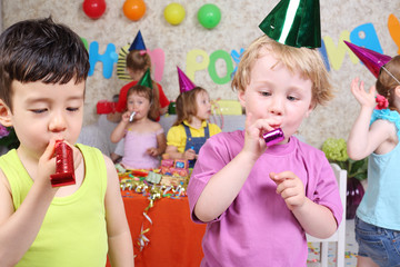 Two little boys blow in multicolor party blowers at birthday