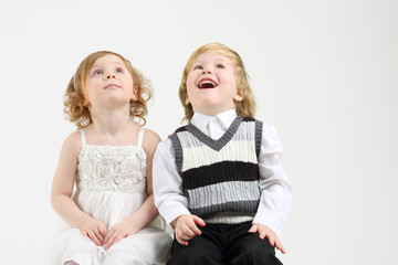 Little happy girl and boy sit on white big cube and look up