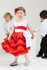 Little girl dances and two boys play behind she on grey