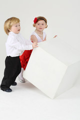 Little boy and pretty girl turn over large white cube