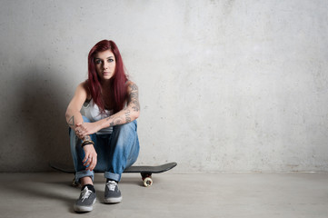 Fototapeta na wymiar Woman with skateboard portrait against concrete wall.