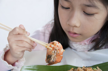Little Asian girl looking at a shrimp in her chopstick.