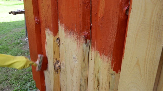 hand yellow glove painting wood plank wall with brush red color