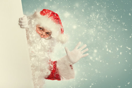 Santa Claus waving hello from behind white blank banner