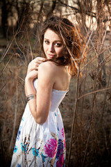 Curly brunette woman in summer dress at forest in sun rays