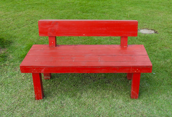 Red wooden bench on the green grass in the park area