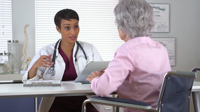 Black doctor talking to disabled elderly woman