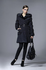 young elegant woman in coat with holding bag posing