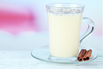 Cup of eggnog with cinnamon on table on bright background