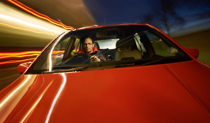 A man driving a red sports car at night.