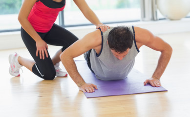 Fototapeta na wymiar Female trainer assisting man with push ups in gym