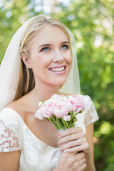 Smiling bride holding her bouquet wearing a veil looking up