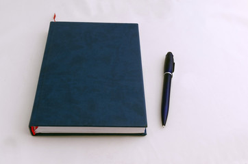 Closed book (notebook) with dark hard-cover and ball-point pen