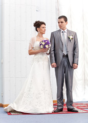 bride and groom holding hands and standing against white wall