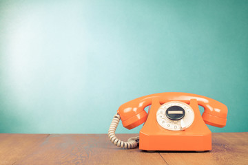 Retro orange telephone on table front mint green wall background
