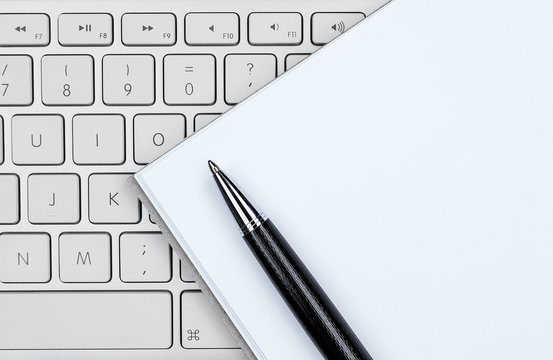Keyboard, white notebook and pen