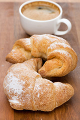 Two fresh croissants and coffee on a wooden background
