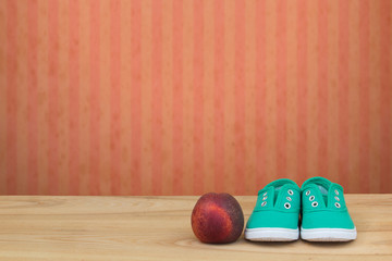 Green sneakers and a peach on a wooden table and red grunge wall