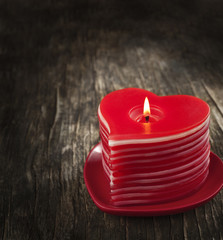 Red burning heart shaped candles on wooden background.