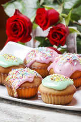Muffins covered with pink icing and colorful sprinkles on wood
