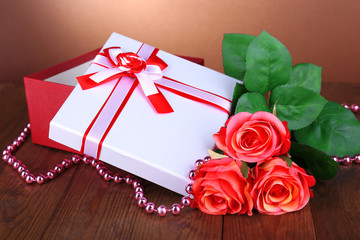 Beautiful gift box with flowers on table on brown background