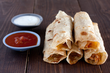 Stack of tortilla flautas with hot sauce and sour cream