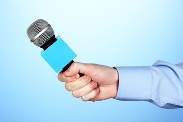 Male hand with microphone on blue background